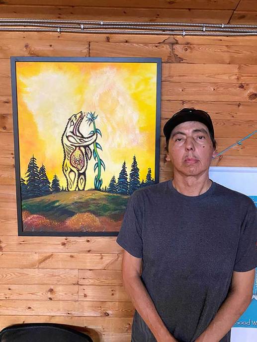 A man poses in front of a painting of a standing bear.